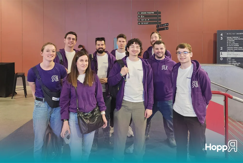 Photo de groupe de neuf membres de l'équipe HoppR portant des vêtements violets aux couleurs de l’entreprise, posant ensemble lors de l'événement DevLille.