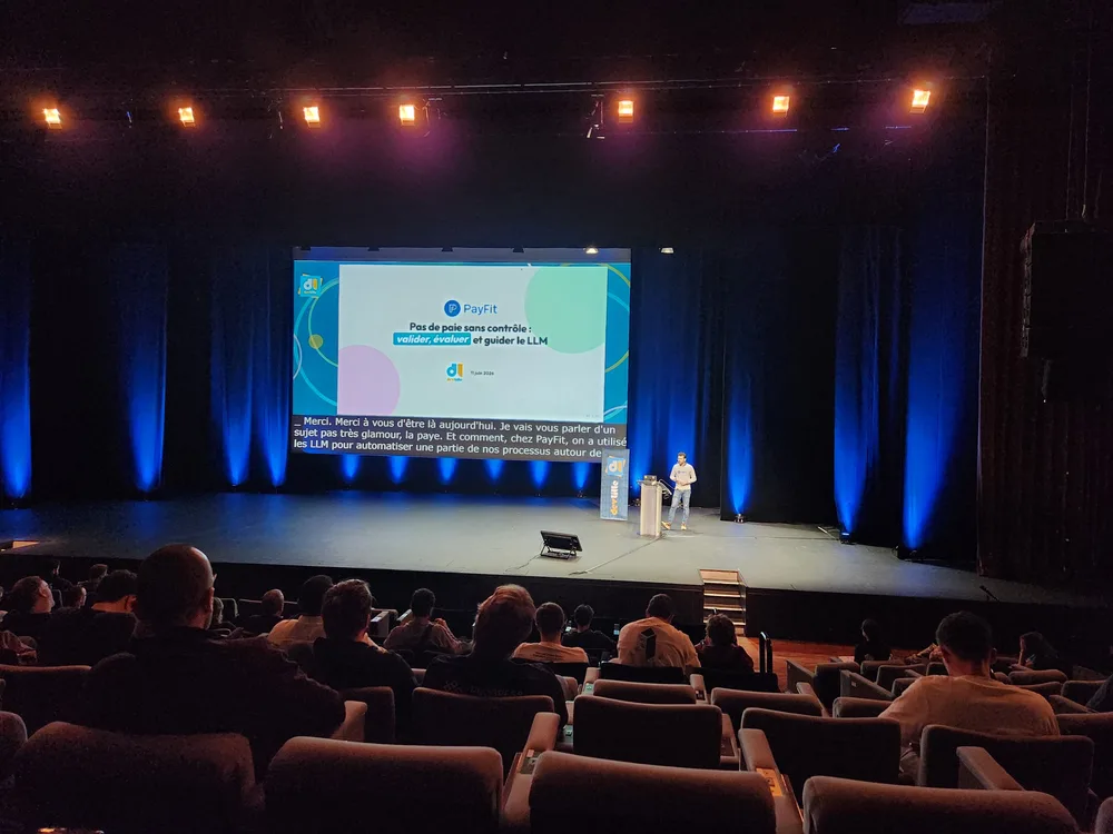 Thomas Villaren sur la scène du Grand Théâtre du Grand Palais à Lille pour Devlille 2026, debout à côté d'un grand écran affichant une présentation PayFit sur les LLM face à un public assis.
