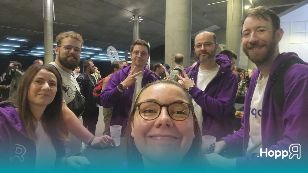 Selfie de groupe de six membres de l'équipe HoppR souriants au DevLille. Ils portent des sweat-shirts violets de l'entreprise et posent ensemble dans le grand hall du centre de conférence.