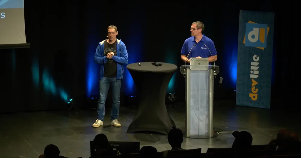 Benoit et Théo présentant sur la scène Marie Curie du Grand Palais  au DevLille, l'un debout près d'une table haute, l'autre au pupitre.